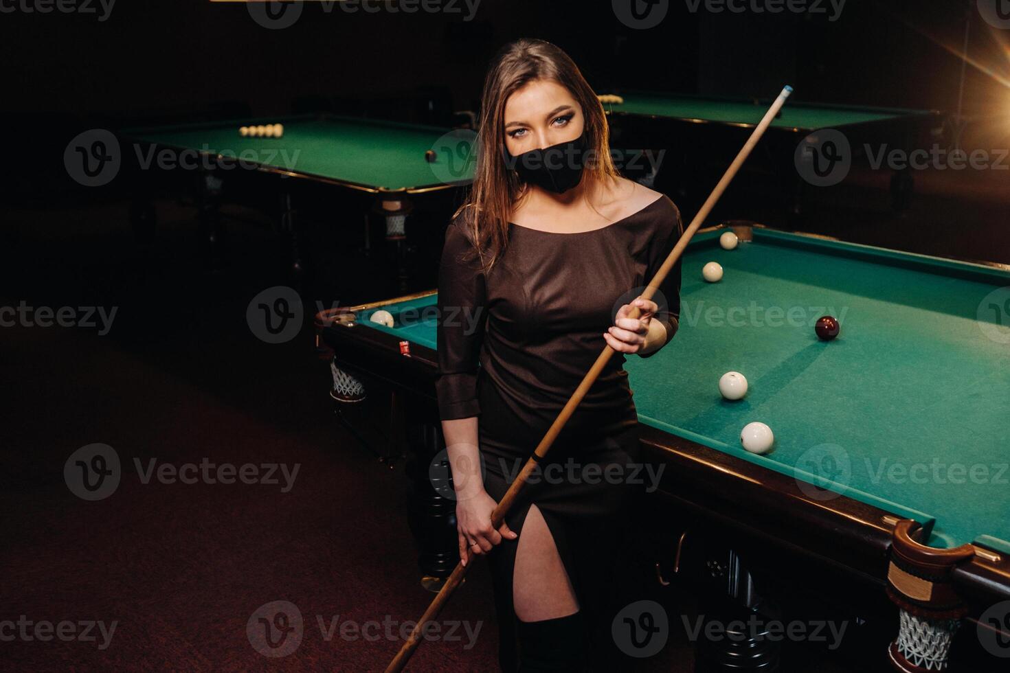 Masked girl in a pool club with a cue in her hands photo