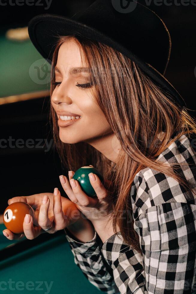 A girl in a hat in a billiard club with balls in her hands.Playing pool photo