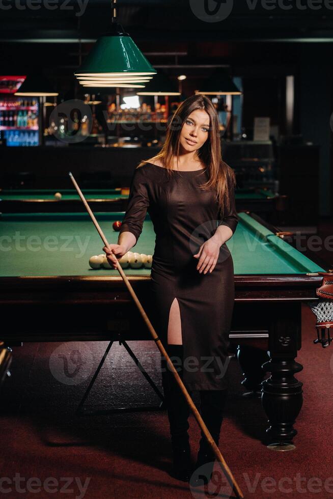 A girl in a hat in a billiard club with a cue in her hands.Pool Game photo