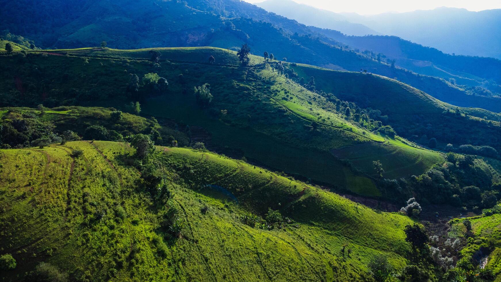 Scenic of idyllic rolling hills landscape with blooming meadows and mountain ranges in the background on a beautiful sunny day with blue sky and clouds in springtime. photo