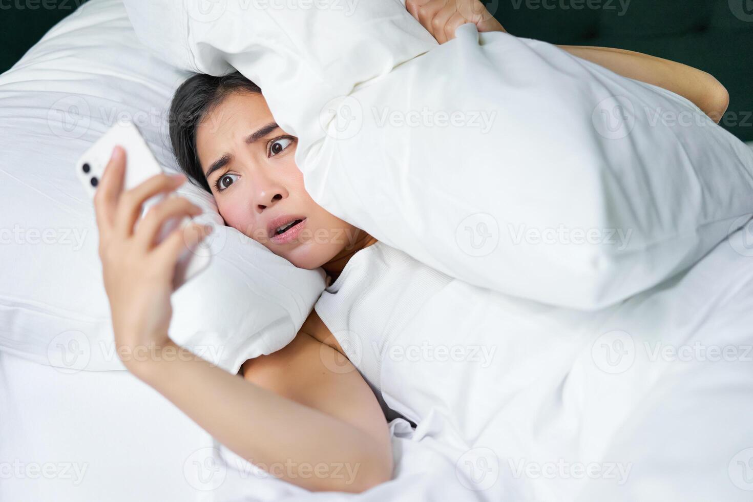 retrato de asiático mujer despertar arriba en cama, mirando conmocionado a móvil teléfono, darse cuenta ella dormido foto