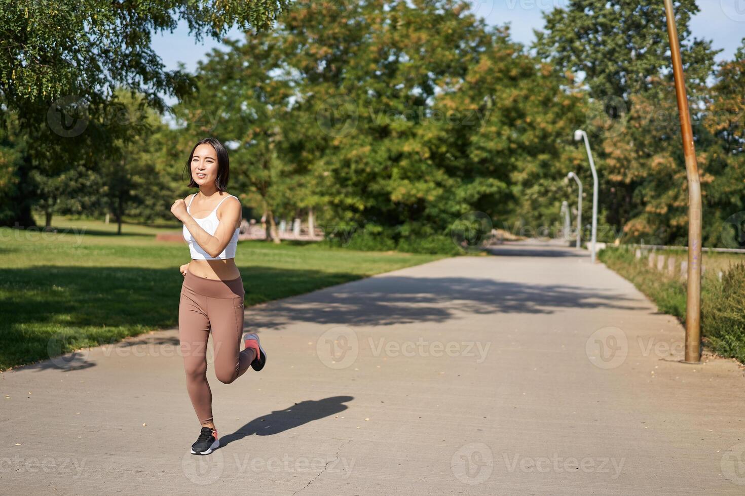 Young asian fitness woman running in park, jogging outdoors, smiling pleased photo