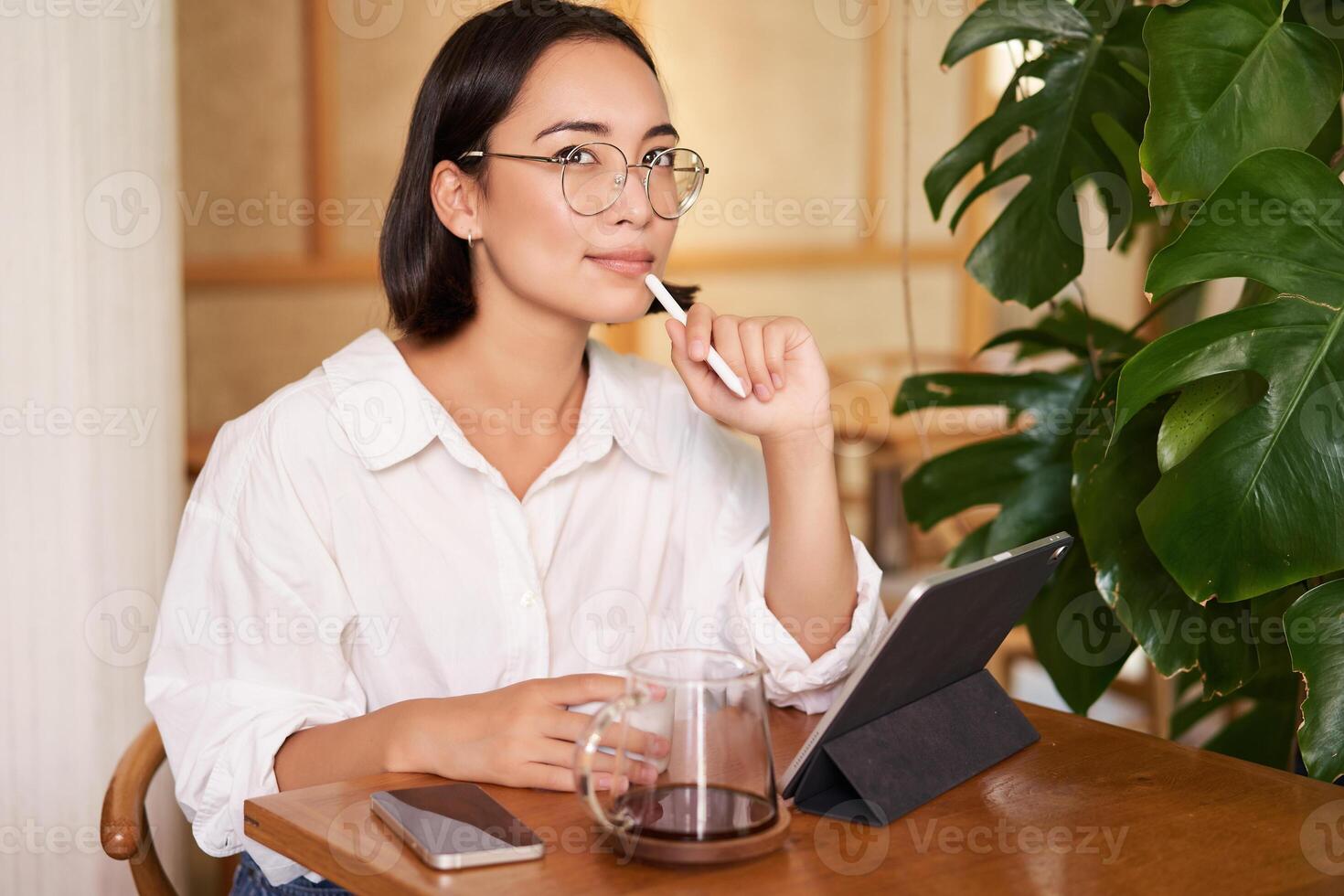 Young artist drawing on digital tablet, using graphic pen, drinking coffee in cafe and scatching smth photo
