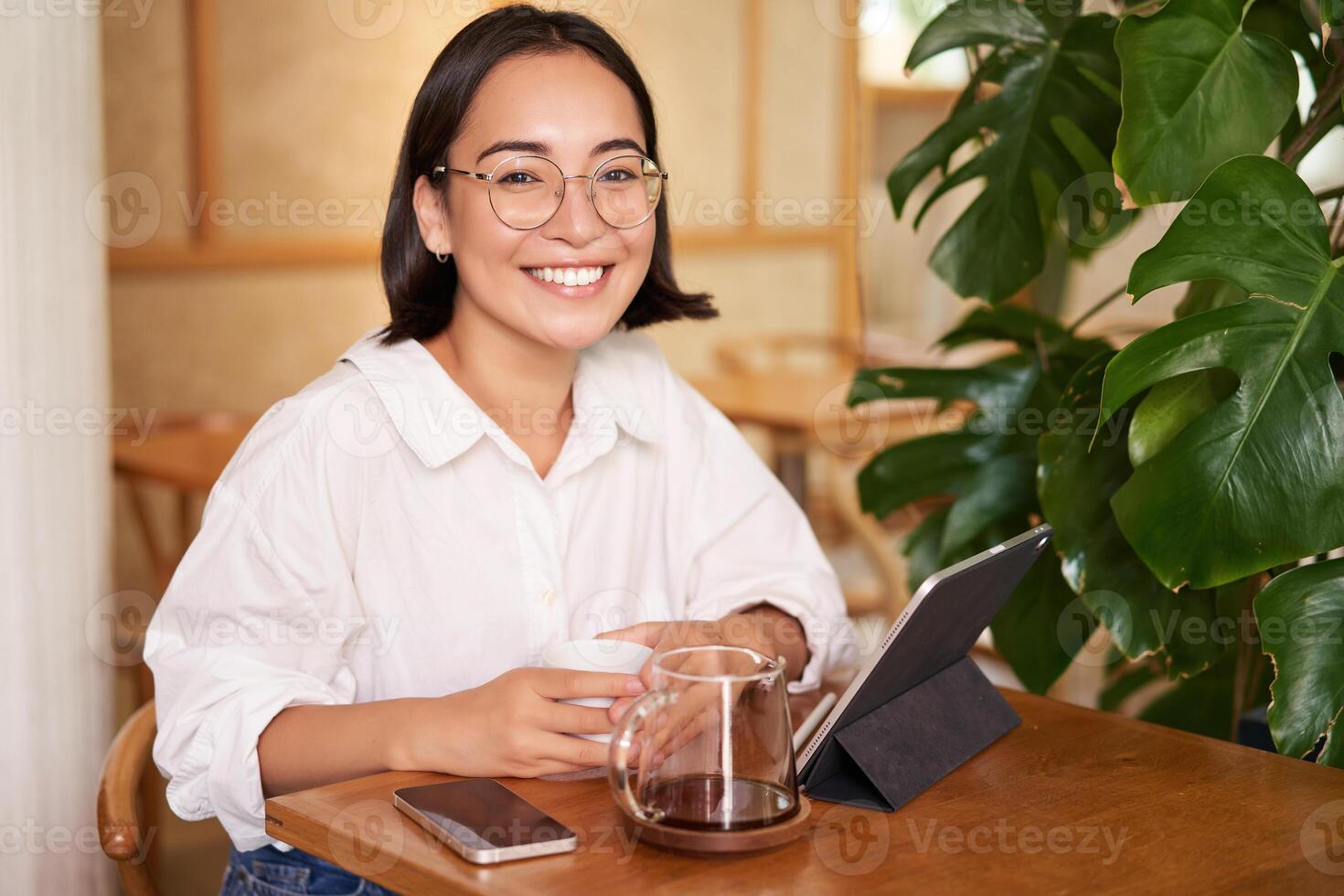 Smiling asian girl in glasses, woman working on remote, drinking coffee and using tablet photo