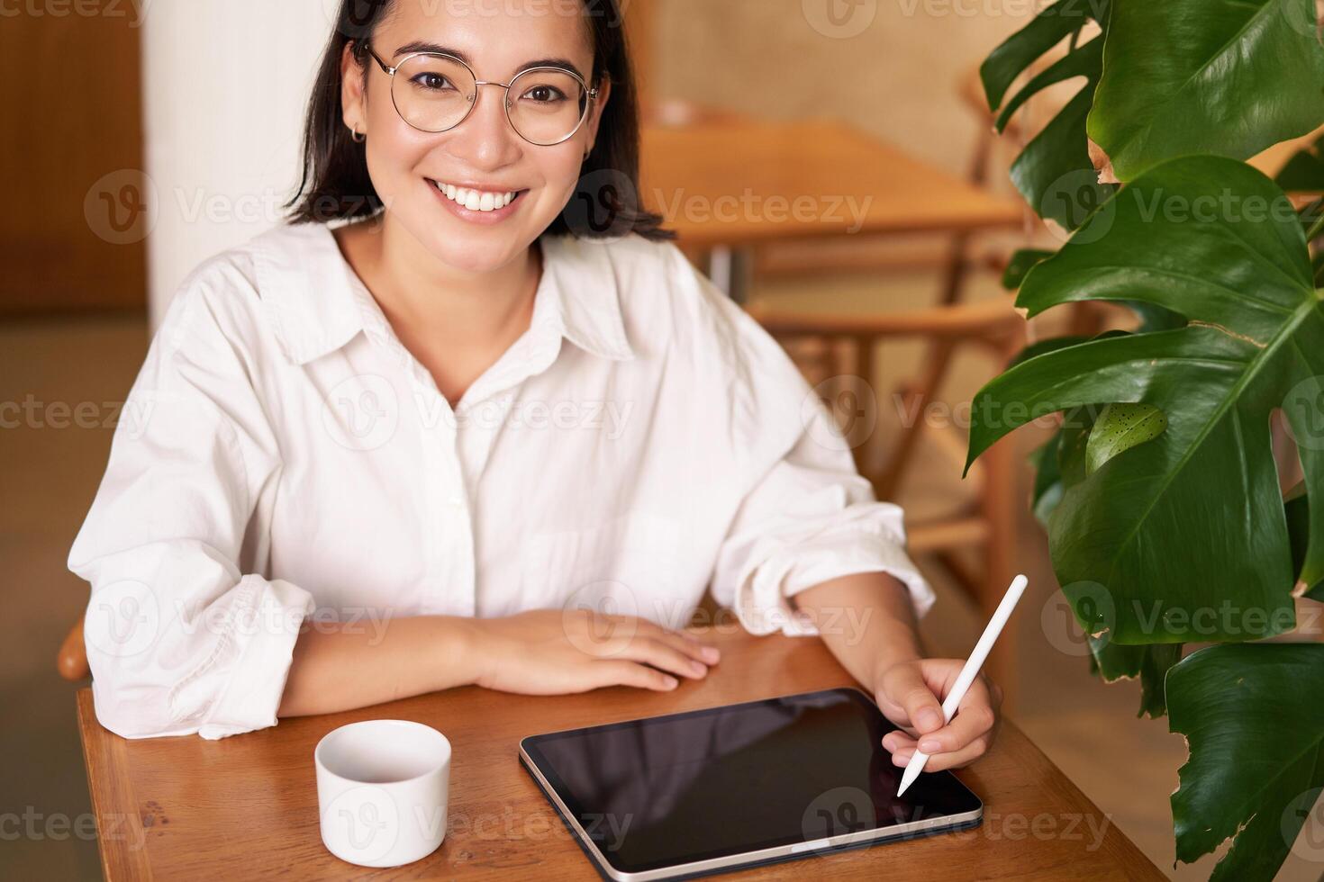 Smiling young female creator, creative girl drawing on digital tablet with graphic pen, drinking coffee in cafe photo