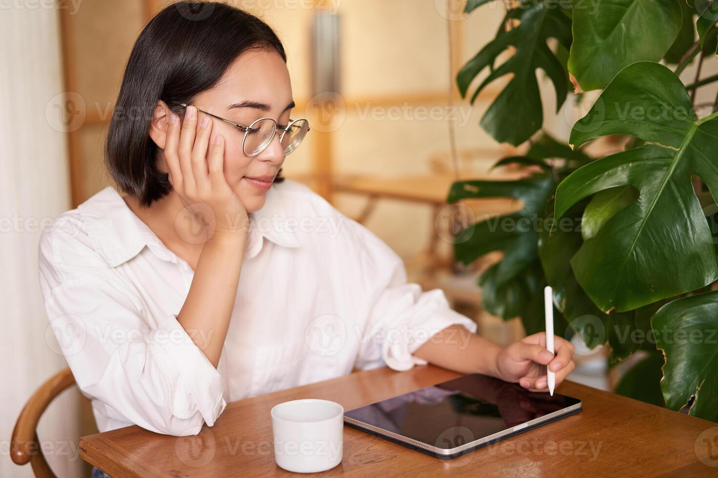 Young artist drawing on digital tablet, using graphic pen, drinking coffee in cafe and scatching smth photo