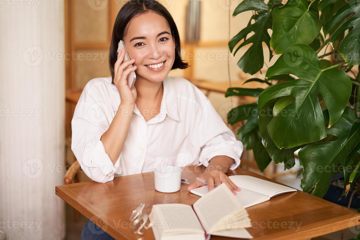 Smiling woman talking on mobile, answer phone call and looking happy, sitting in cafe photo