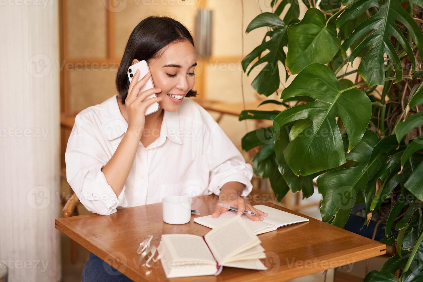 Working woman answer phone call in cafe, writing down, making notes while having conversation on telephone photo