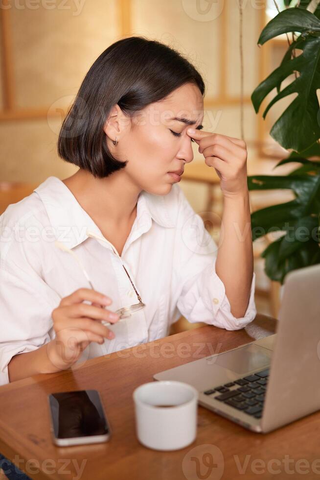 Working woman feeling tired, rubbing eyes after using laptop, having fatigue, sitting in cafe with coffee photo