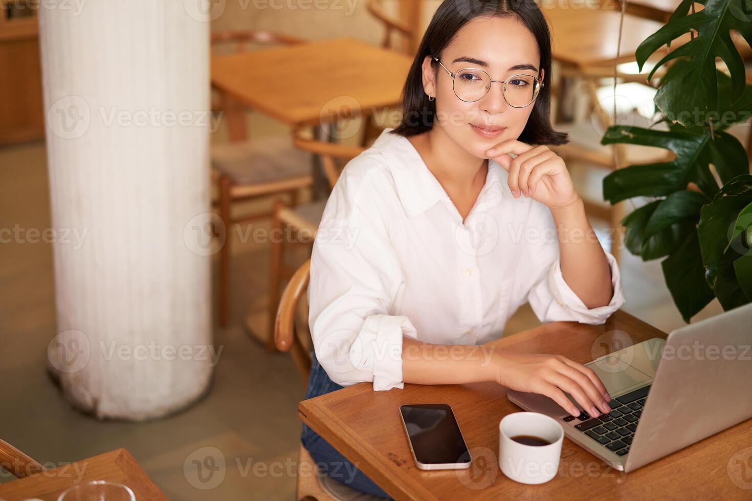 Working female entrepreneur sitting in cafe with laptop, typing on computer, drinking coffee photo