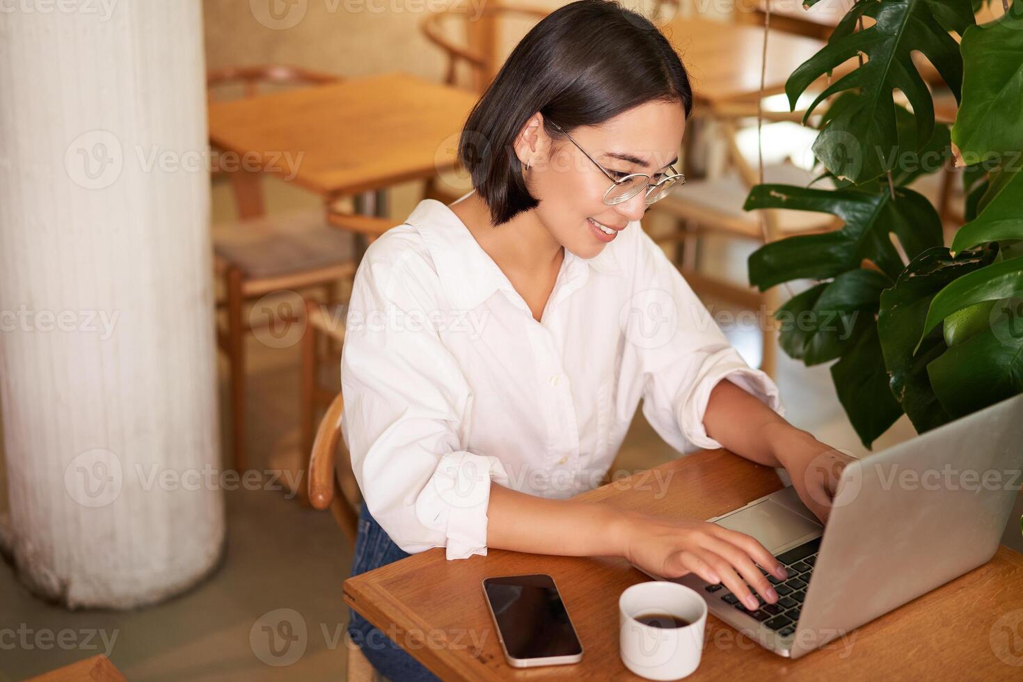 Working female entrepreneur sitting in cafe with laptop, typing on computer, drinking coffee photo
