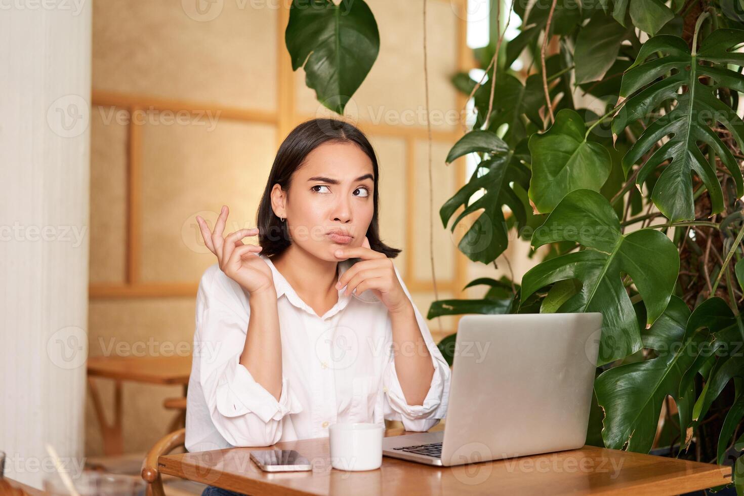 Young businesswoman thinking, frowning as sitting puzzled and complicated, using laptop in cafe photo