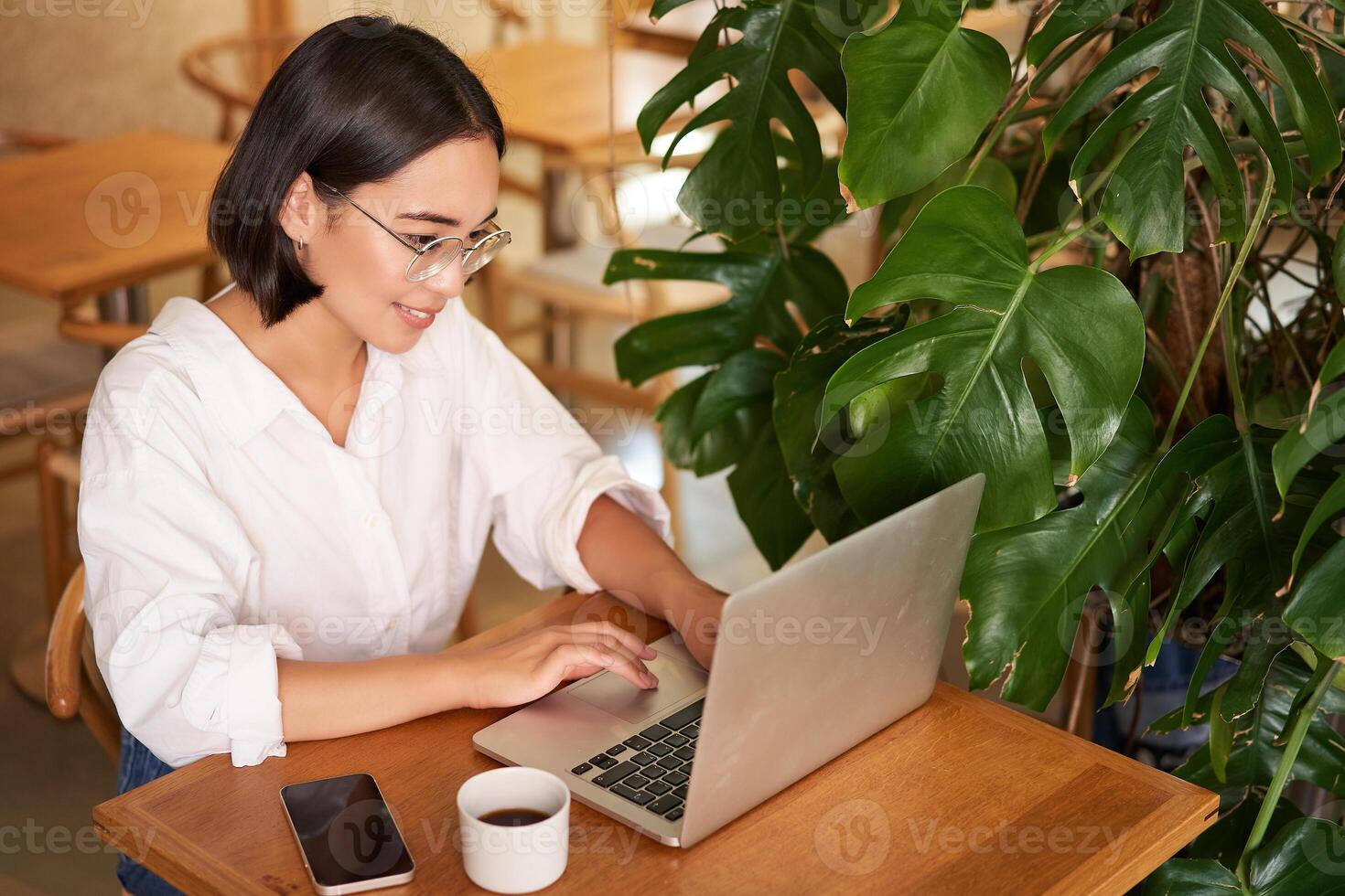 Working female entrepreneur sitting in cafe with laptop, typing on computer, drinking coffee photo