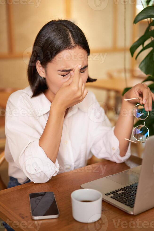 Working woman feeling tired, rubbing eyes after using laptop, having fatigue, sitting in cafe with coffee photo