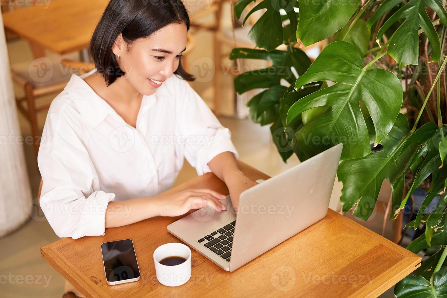 Working woman in cafe, using laptop, studying remotely, freelancing from restaurant, drinking coffee photo