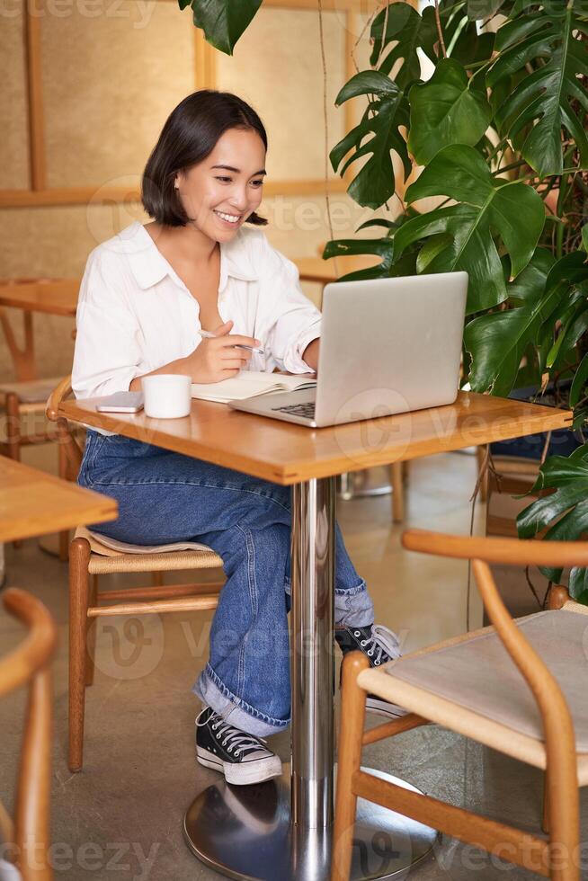 Stylish businesswoman with laptop, sitting in cafe and working on computer, managing business and drinking coffee photo