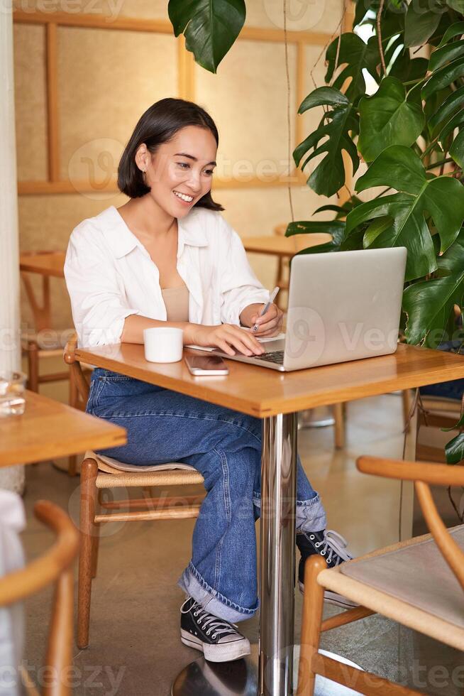 Stylish businesswoman with laptop, sitting in cafe and working on computer, managing business and drinking coffee photo