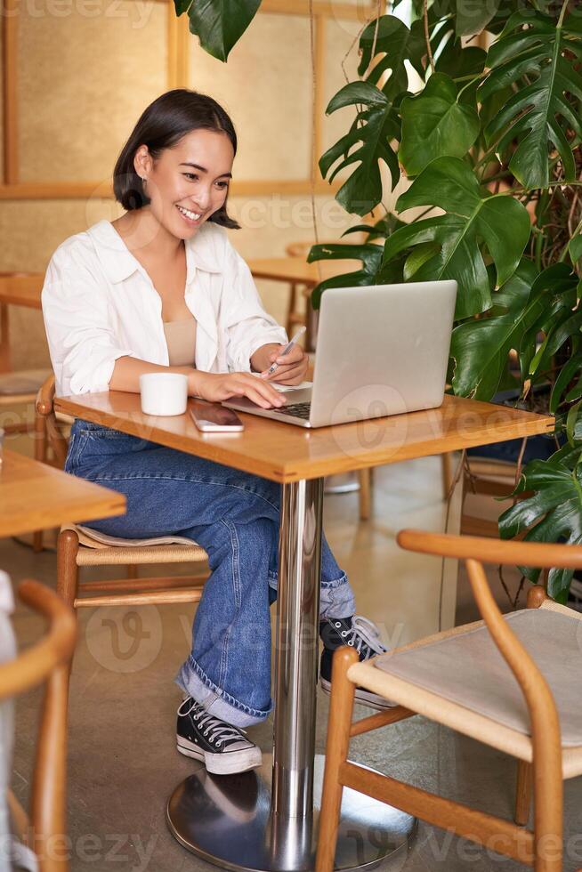 Stylish businesswoman with laptop, sitting in cafe and working on computer, managing business and drinking coffee photo