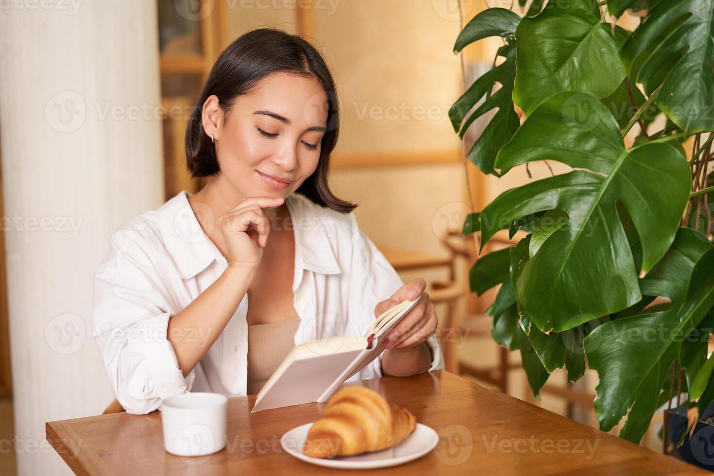 Smiling beautiful girl with a book, reading with thoughtful smirk, thinking of something, drinking coffee in cafe photo