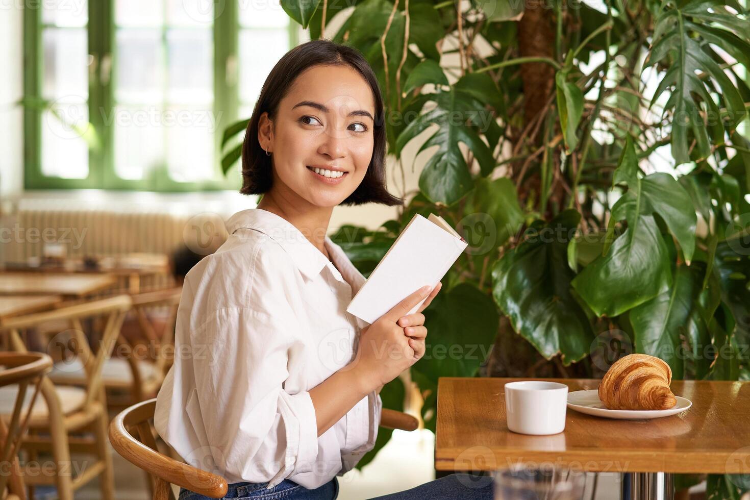 Tender, beautiful asian girl sitting with a book in cafe, reading and drinking coffee. People and lifestyle concept photo