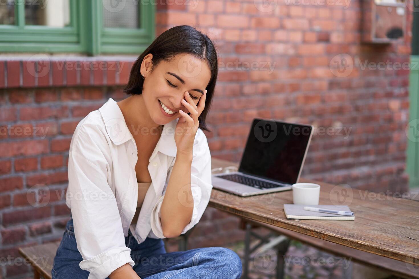 Beautiful korean girl with laptop, sitting in outdoor cafe, drinking coffee and using computer photo