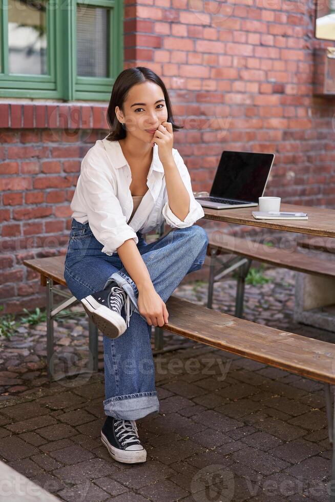 Vertical shot of trendy asian girl sitting in cafe alone with laptop, working or studying, browsing on computer photo