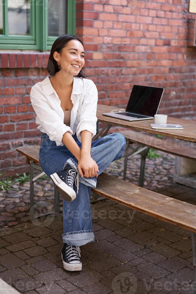 Vertical shot of trendy asian girl sitting in cafe alone with laptop, working or studying, browsing on computer photo