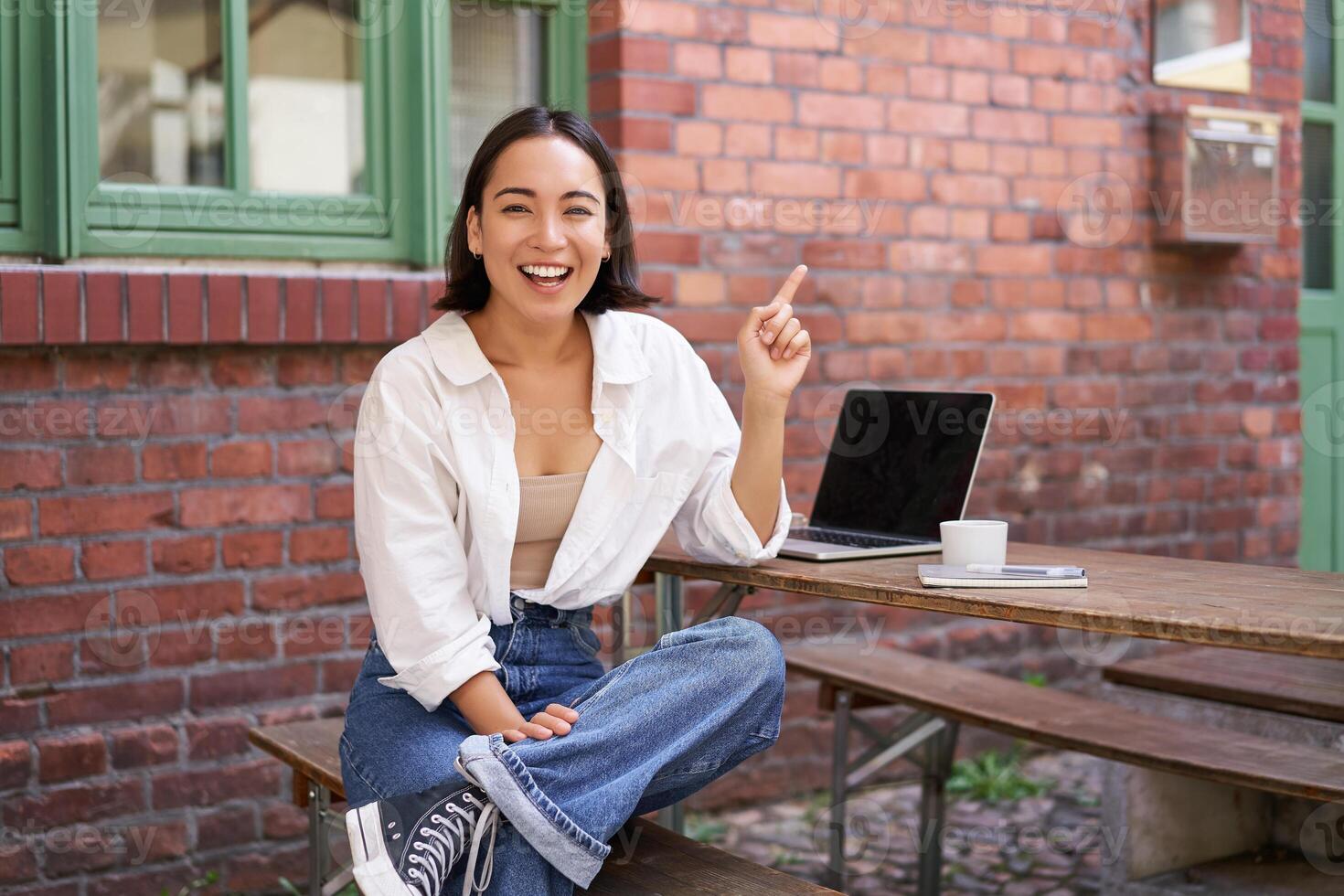 Enthusiastic asian woman, pointing at upper right corner, showing advertisement, news on banner, looking impressed and intrigued by smth photo