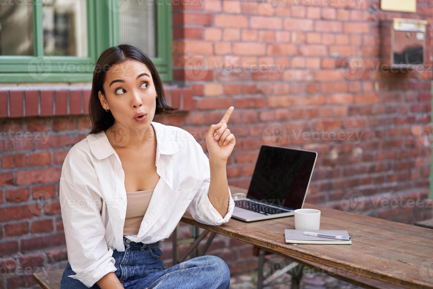 Enthusiastic asian woman, pointing at upper right corner, showing advertisement, news on banner, looking impressed and intrigued by smth photo