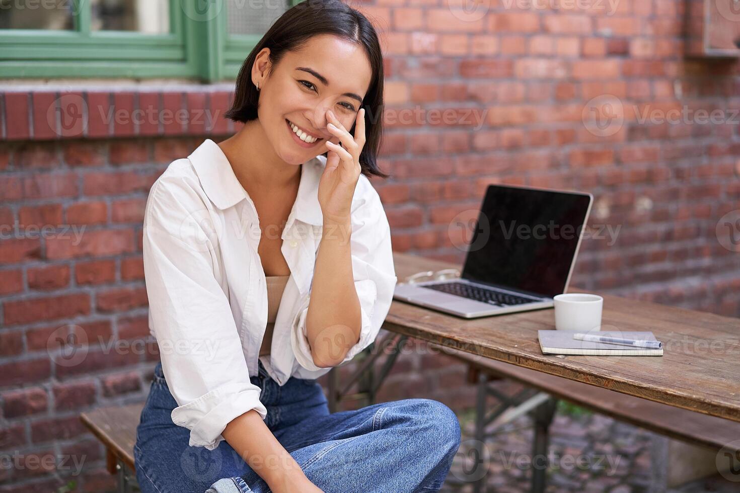 Beautiful korean girl with laptop, sitting in outdoor cafe, drinking coffee and using computer photo