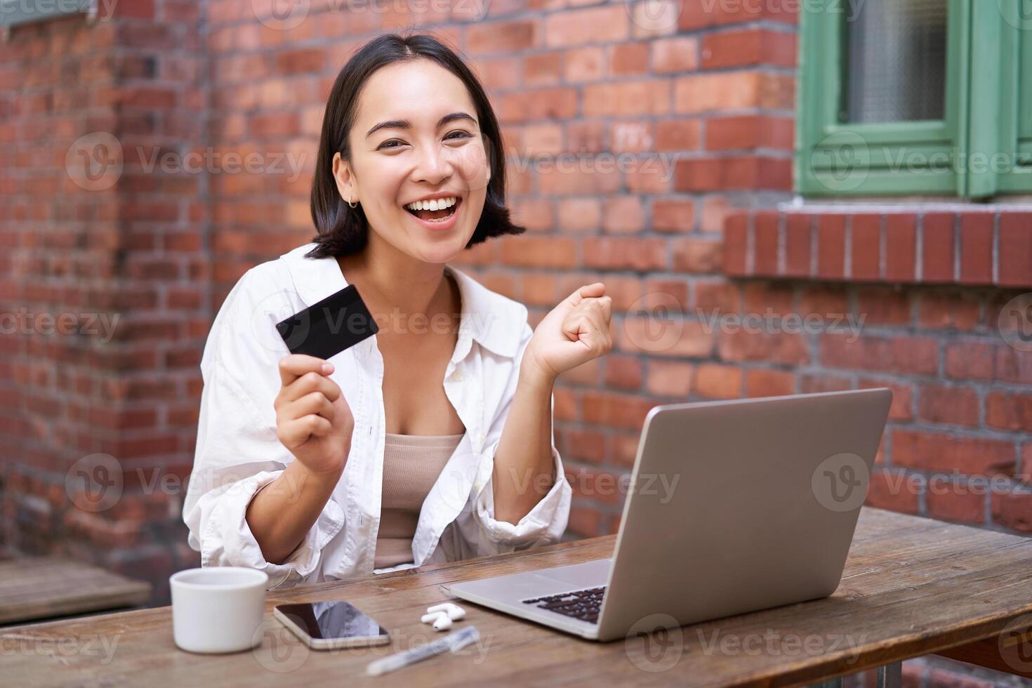 Enthusiastic asian girl sitting with credit card and laptop, paying contactless, shopping online via computer photo