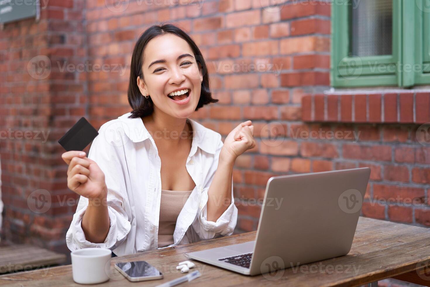Enthusiastic asian girl sitting with credit card and laptop, paying contactless, shopping online via computer photo