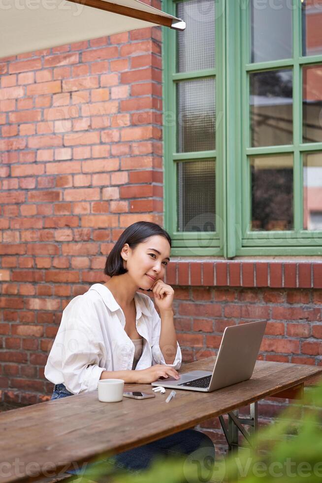 Beautiful brunette woman sitting outdoors and using laptop, chatting online, working with computer outside office photo