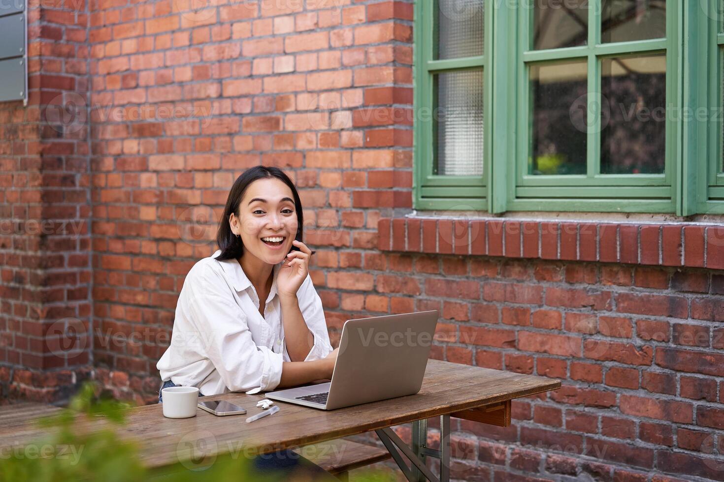Enthusiastic asian woman sitting with laptop, laughing and smiling, looking happy, working remote online photo