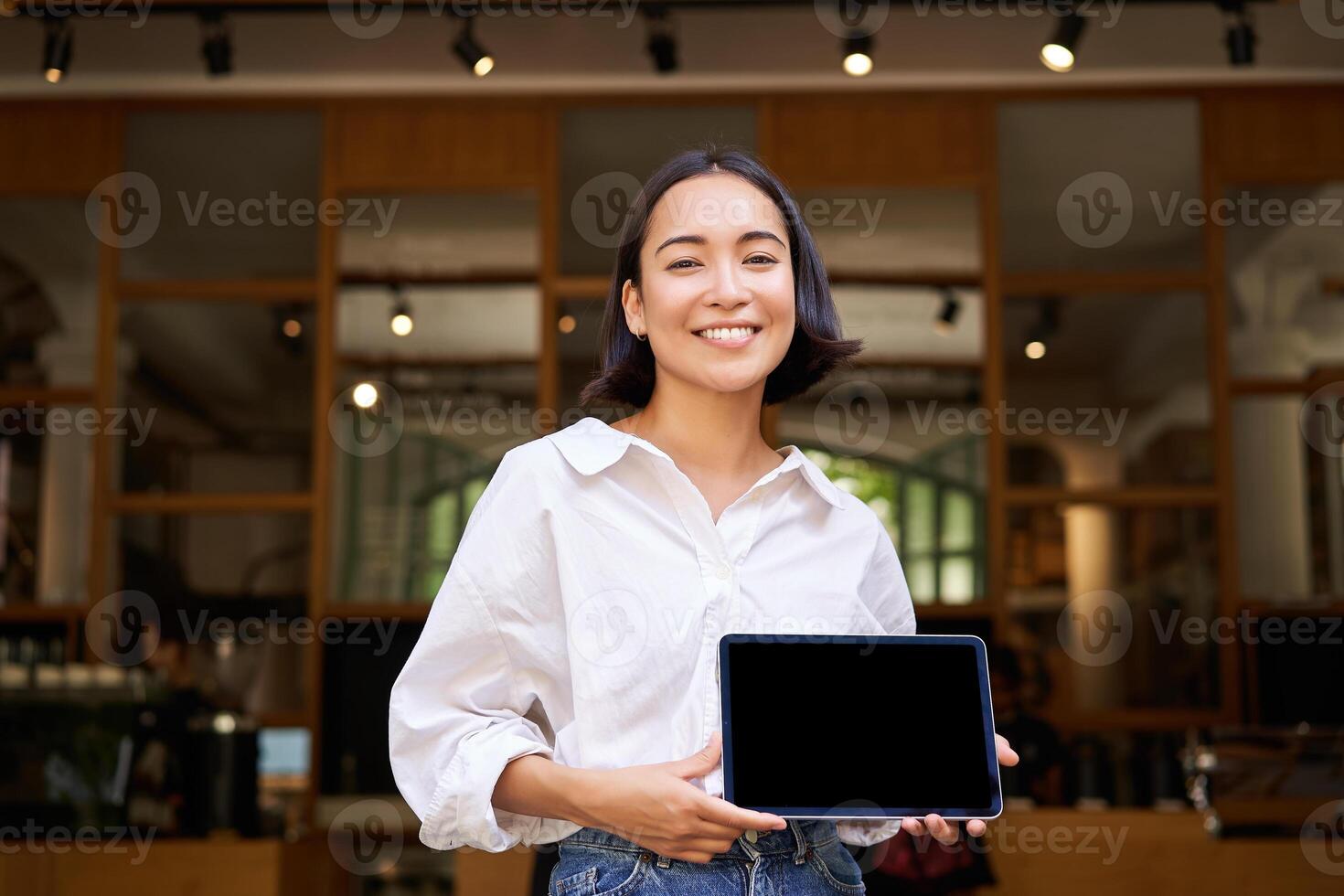 Cheerful young restaurant administrator, asian girl shows digital tablet and smiling photo