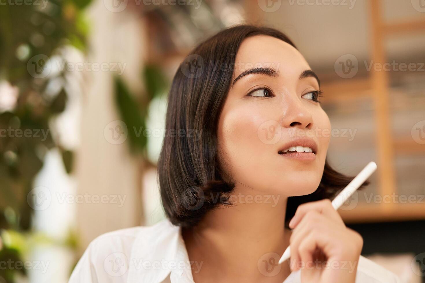 Close up portrait of stylish young brunette woman, sitting with graphic pen and smiling, relaxing in cafe, writing something, making notes photo