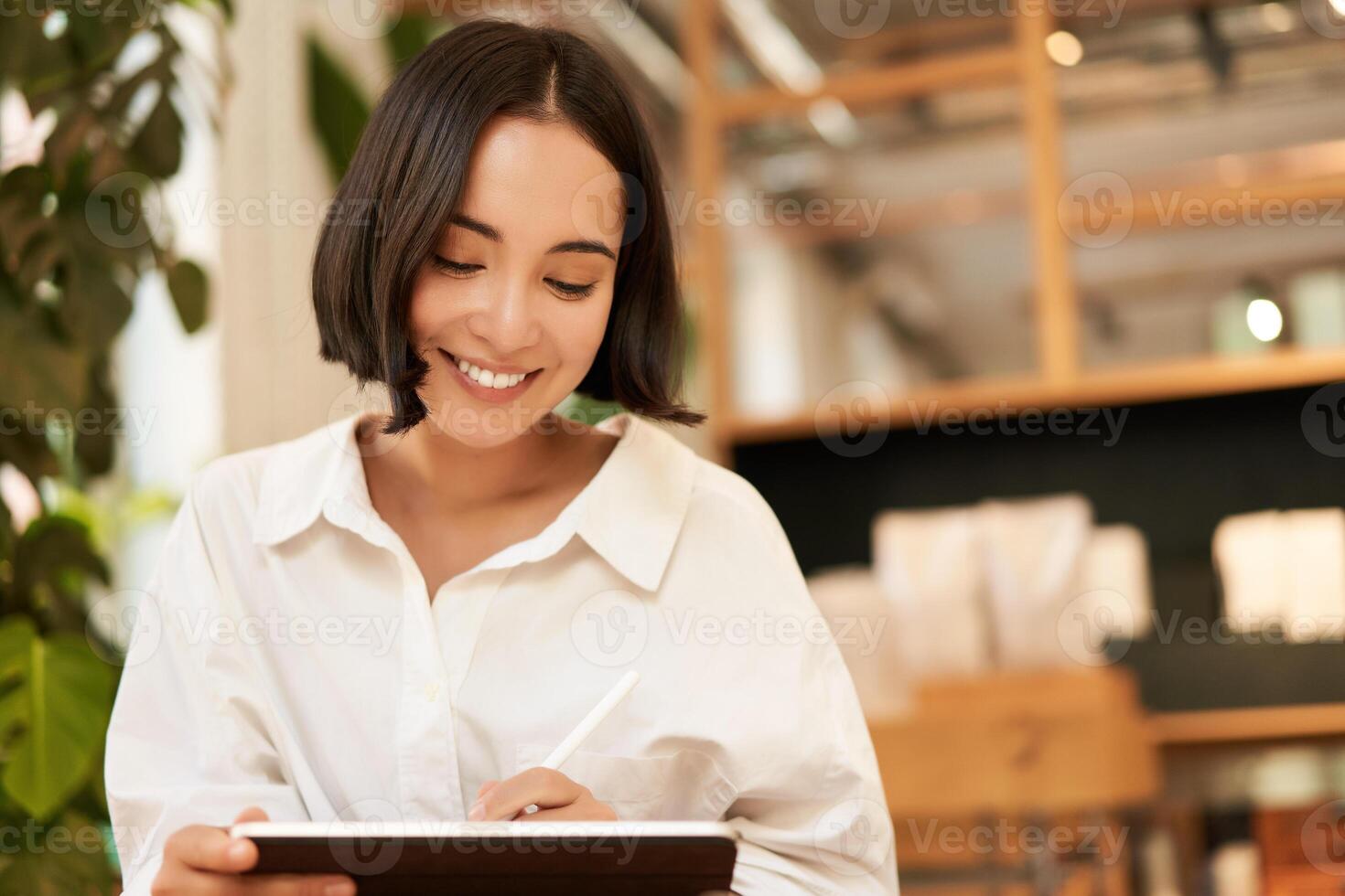 Portrait of asian girl drawing on digital tablet, scatching and doodling with graphic pen, sitting in cafe and smiling photo