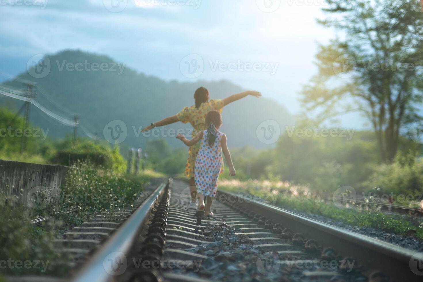 Mother and cute daughter walking on the railroad in the daytime. Happy family walking on the railway against the background of mountains and greenery. photo