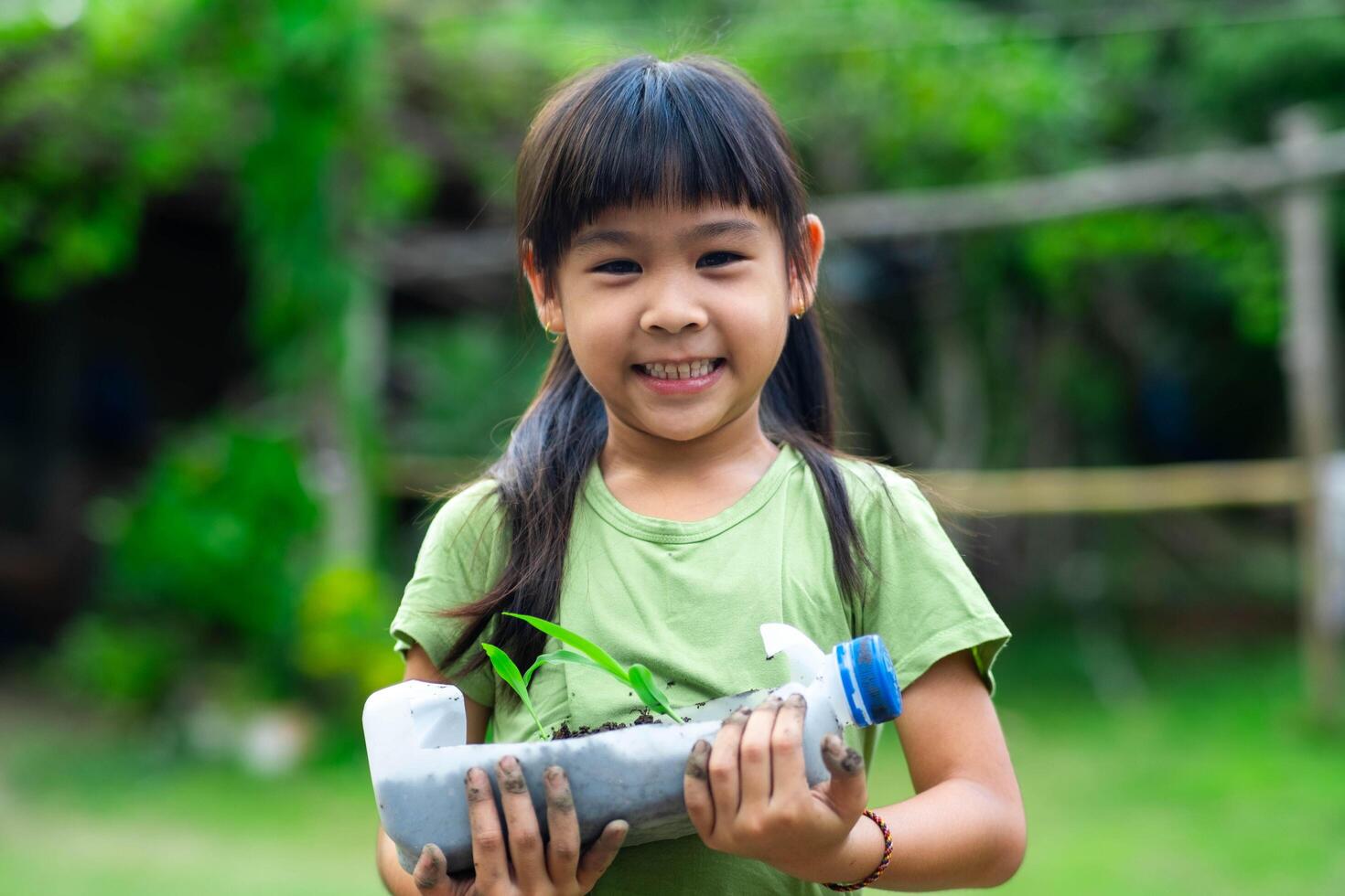 Little girl shows saplings grown in recycled plastic bottles. Recycle water bottle pot, gardening activities for children. Recycling of plastic waste photo