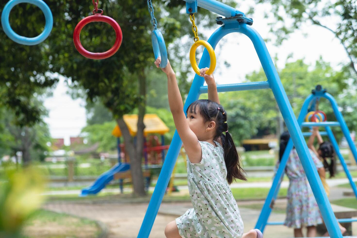 Happy girl hanging on monkey bar by hand doing exercise. Little Asian girl playing at outdoor playground in the park on summer vacation. Healthy activity. photo