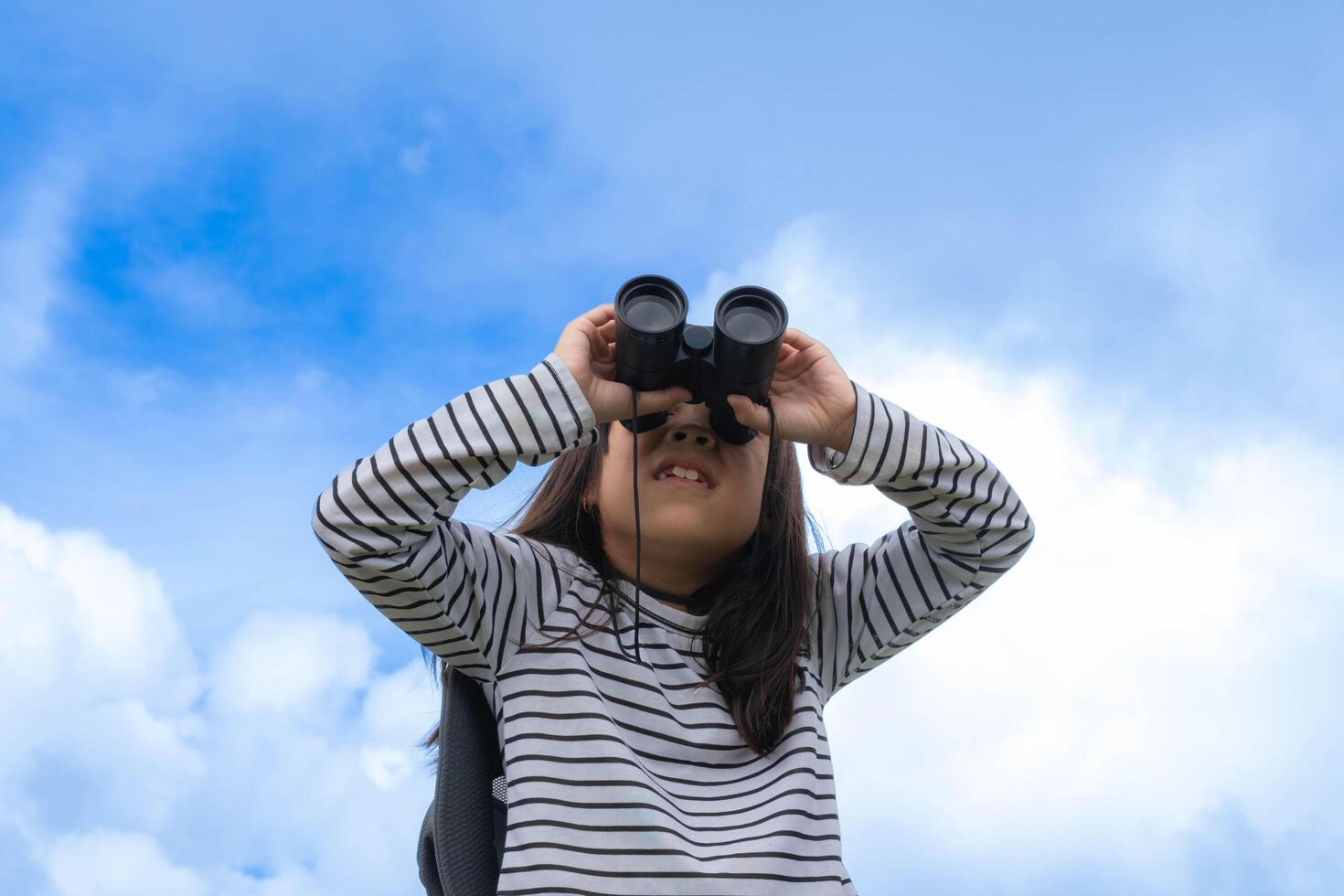 Cute little girl with binoculars on the mountain on a sunny day. Young girl uses binoculars when going hiking. Active young girl uses binoculars on a trip and smiles happily. photo