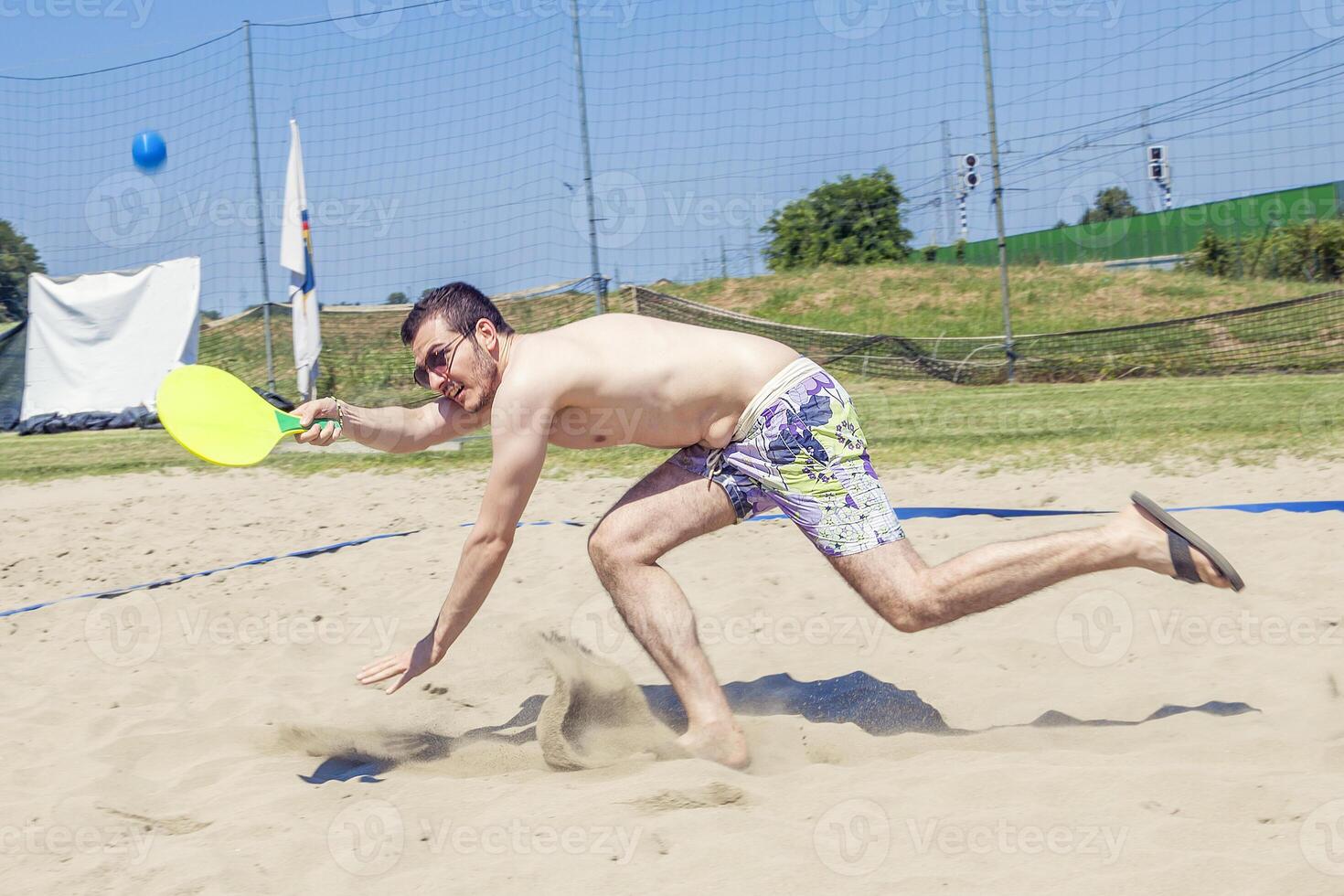 Young adult man plays tennis on the beach photo