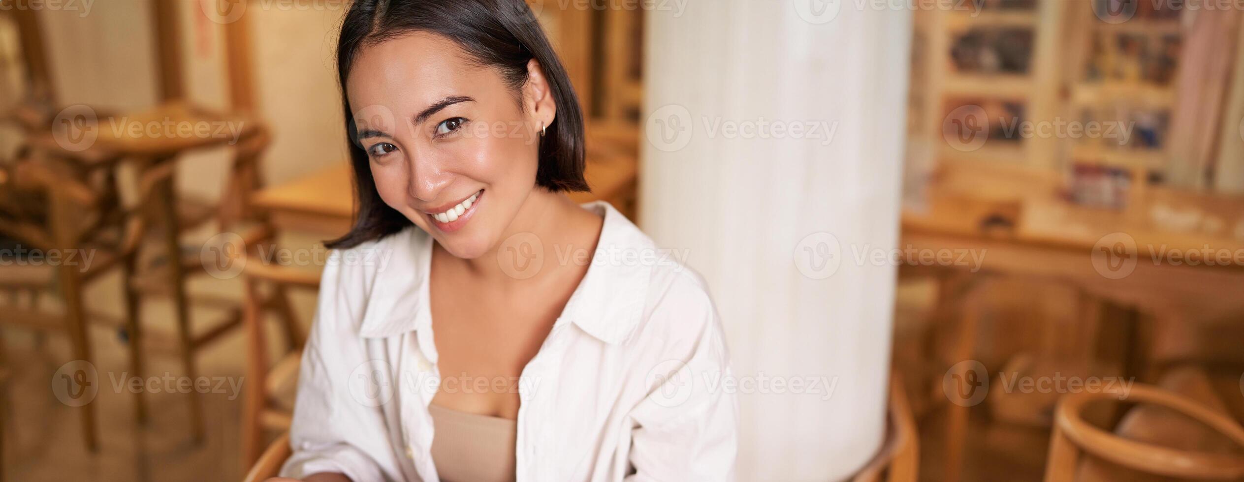 Vertical shot of young smiling woman with book, reading in cafe, enjoying morning breakfast coffee and croissant photo