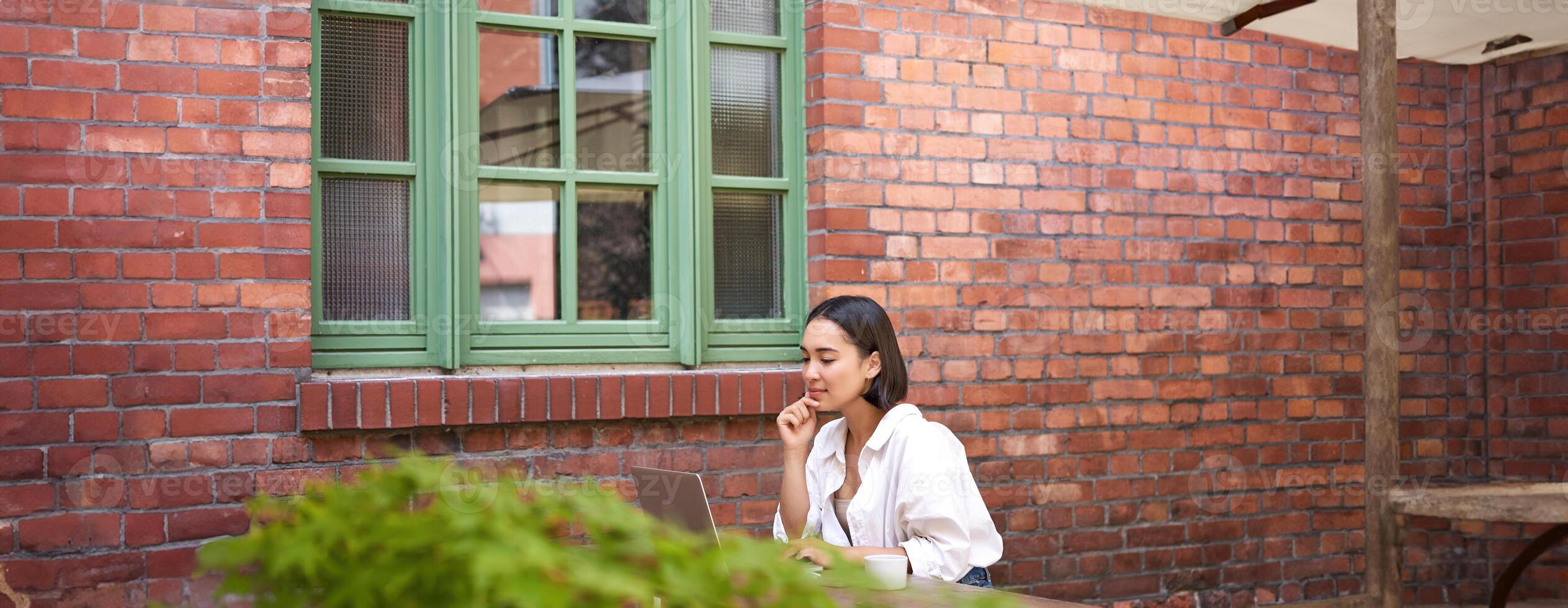 Beautiful brunette woman sitting outdoors and using laptop, chatting online, working with computer outside office photo