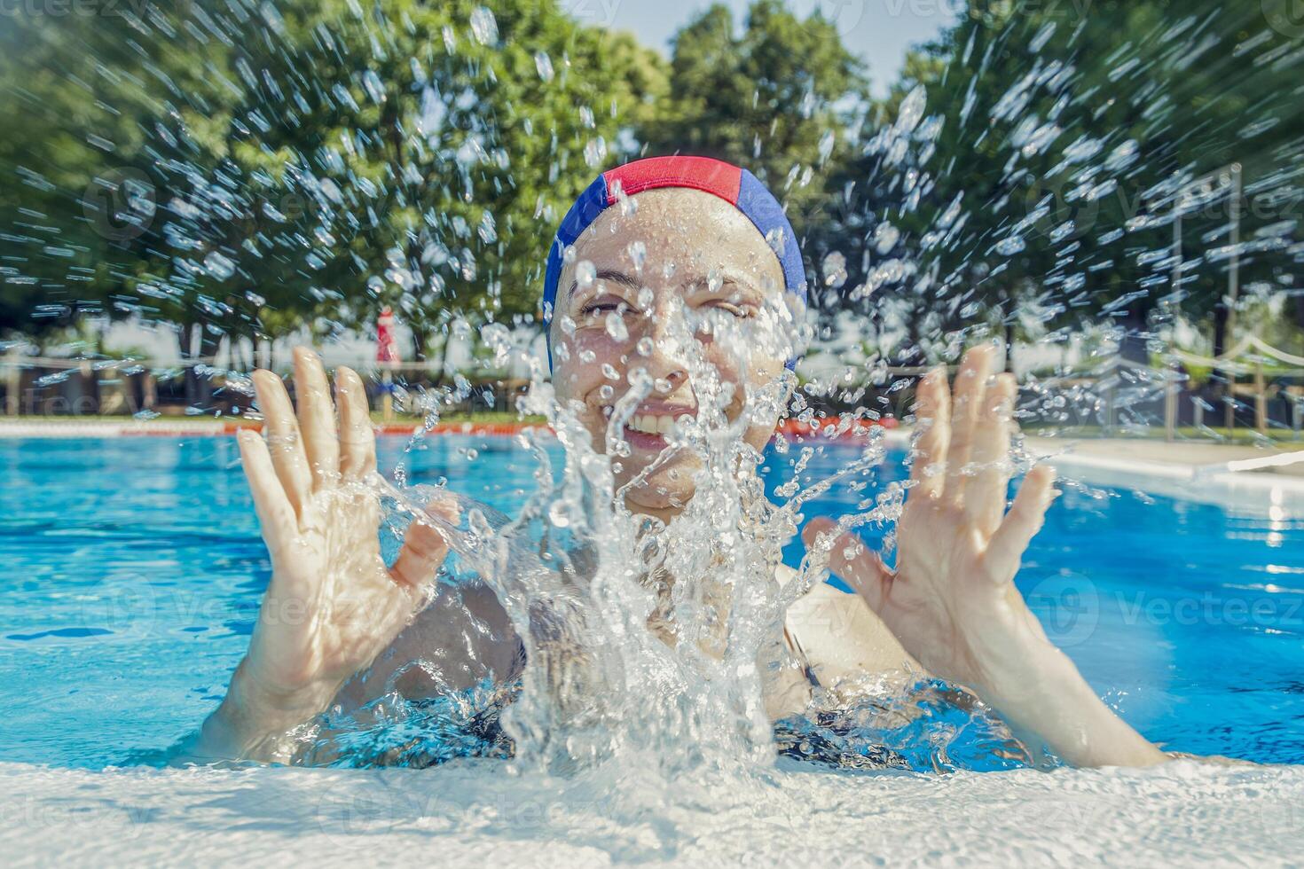 bonito niña vistiendo un piscina gorra a el junto a la piscina salpicaduras agua foto