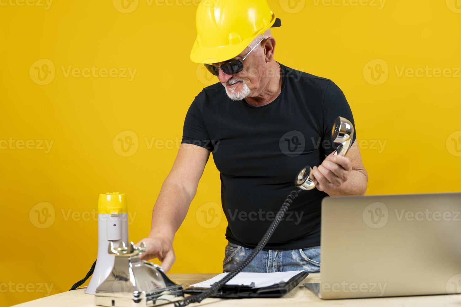 trabajador en un espartano oficina es vocación con un cromo teléfono aislado en amarillo antecedentes foto