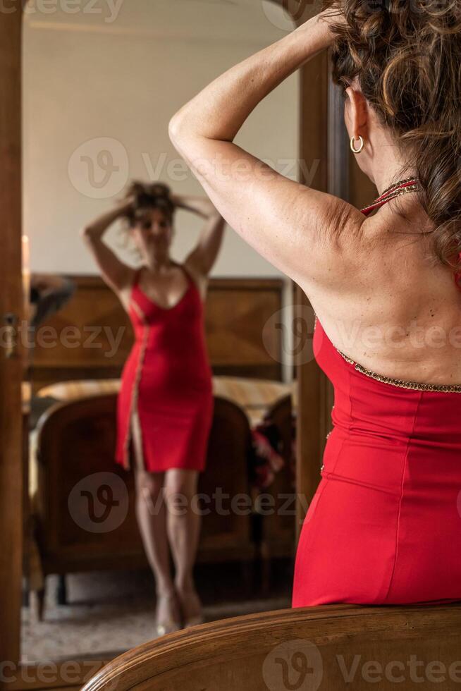 attractive middle aged woman wearing a red dress in front of the mirror photo