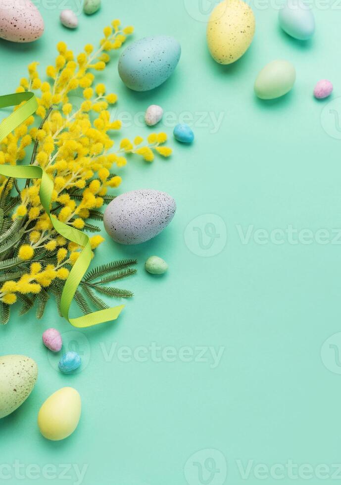 Festive Easter Decoration With Colorful Eggs and Mimosa Flowers on a Pastel Green Background photo