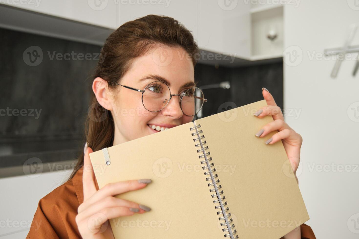 Portrait of beautiful young woman studying, student revising at home, doing homework, holding planner, reading her notes and smiling, writing in diary photo