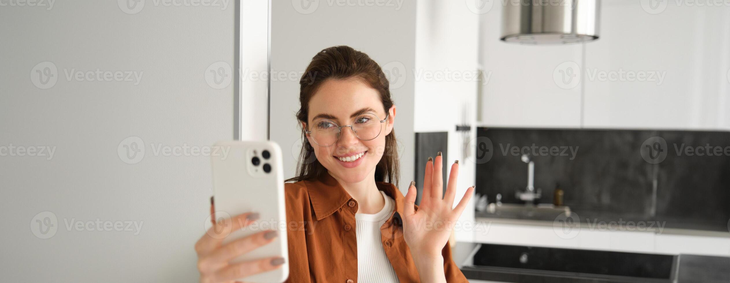 retrato de elegante hermosa mujer a hogar, vídeo chats en teléfono inteligente, conecta a en línea reunión desde su vivo habitación, estilo de vida social medios de comunicación blogger registros un vídeo en móvil teléfono foto